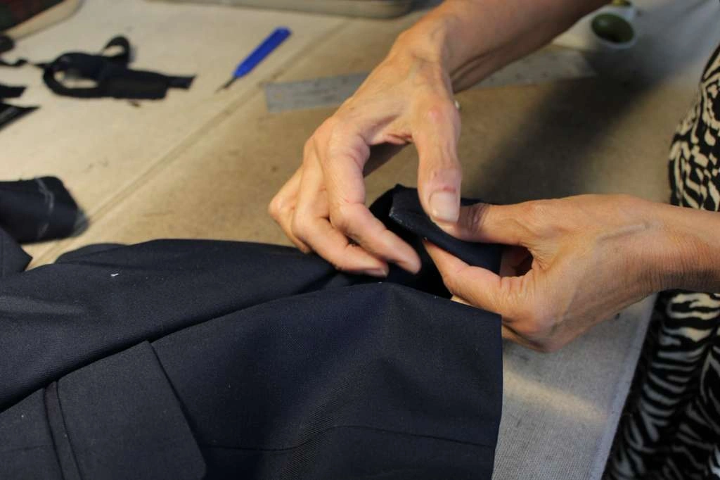 An expert tailor measuring and folding fabric with tailor chalk marks on a workspace table at Precision Alterations Phoenix.